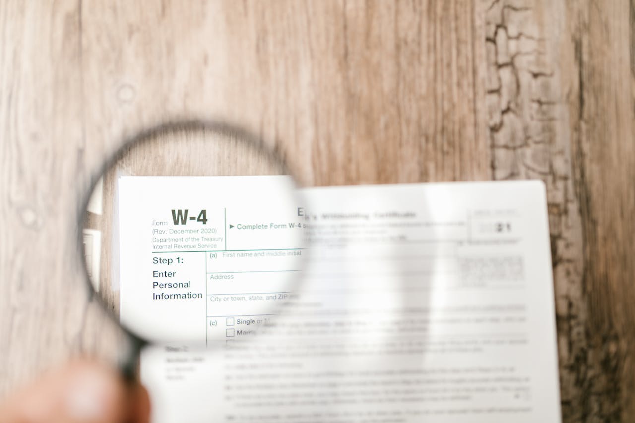 services-05 Close-up of a W-4 tax form through a magnifying glass on a wooden table.